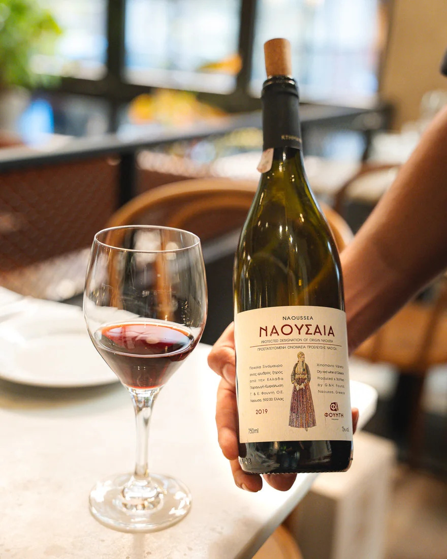 Flaska rött Naoussa-vin på Xinomavro och ett glas vid bordet